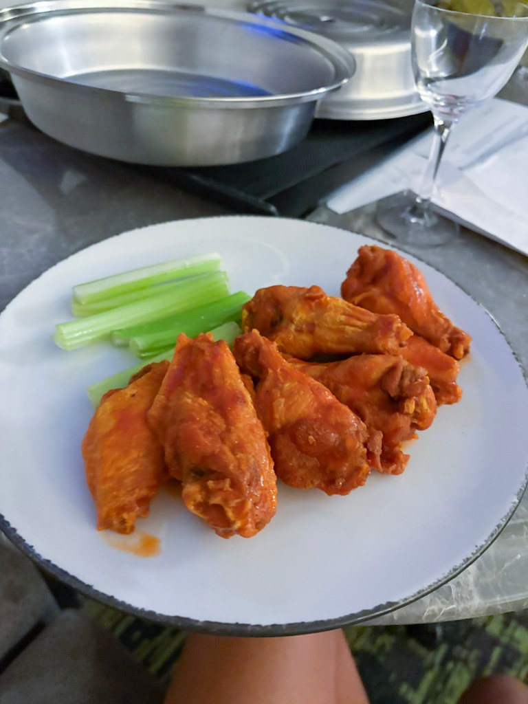 A plate of spicy buffalo chicken wings served with celery sticks, set on a table with a blurred background.